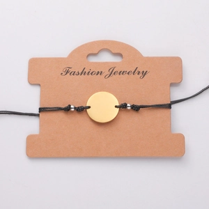 Detail of adjustable black cord bracelet with a polished gold circular charm on display card