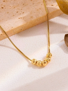 Detail of a gold box chain necklace with five geometric engraved beads on a stone