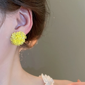 Nahaufnahme von gelben Kristall-Ohrsteckern in Blumenform getragen von einem Model