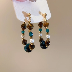 Detailed close-up of tiger eye stone and drop pearl hoop earrings with golden beads