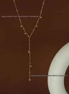Detailed view of long Y-shaped gold tassel necklace with polished beads on a dark background
