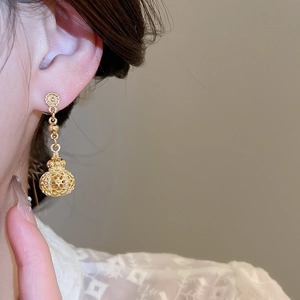 Close-up of golden hollow lantern drop earrings with flower stud on ear