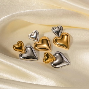 Detailaufnahme der herzförmigen Ohrringe in Gold-Silber-Kontrast auf Seidenstoff