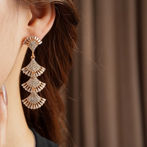 Close-up of golden tiered fan tassel earrings with sparkling crystals on a female model