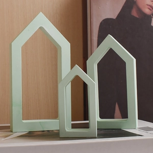 Three mint green minimalist house-shaped plaster ornaments on a light wood background