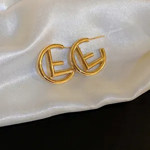 Golden C-shaped hollow letter earrings with needle stud on white silk background