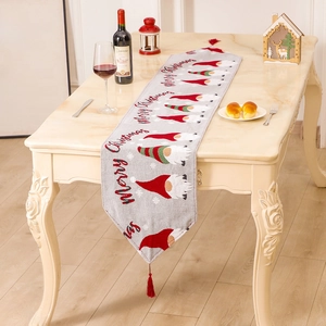 Christmas table runner with gnome jacquard and red tassels on white wooden table