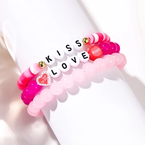 Macro shot of handmade beaded bracelets set featuring pink hearts and KISS LOVE text