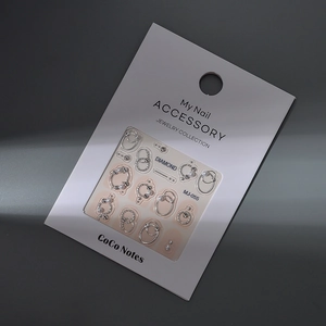Détail de bijoux d'ongles avec anneaux argentés, perles et strass sur carte MJ-055