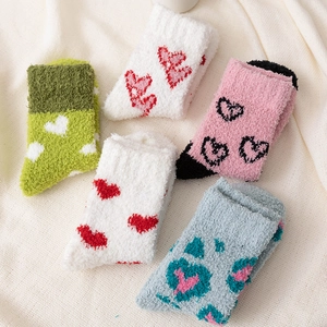 Five pairs of coral fleece socks with heart patterns on a soft beige background