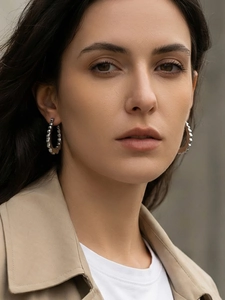 Close-up of textured silver U-shaped hoop earrings worn by a model in beige coat