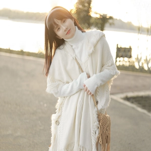 Bohemian white knit poncho with buttons and fringe details shown in warm outdoor lighting