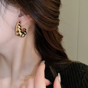Detailed close-up of golden C-shaped hoop earrings with spiral texture on a model