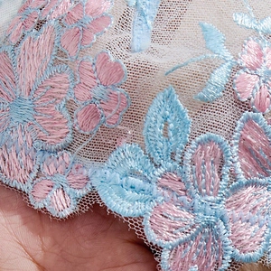 Detailed macro view of delicate pink and blue floral embroidery on sheer white lace fabric