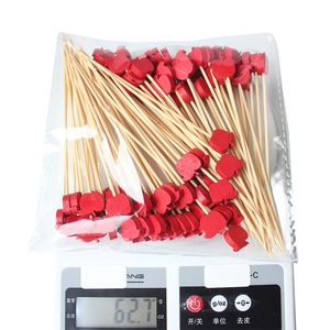 Bamboo fruit picks with red apple toppers on a scale for weighing 100 pieces