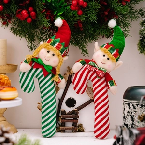 Christmas elf candy cane ornaments in red and green fabric leaning on wooden house