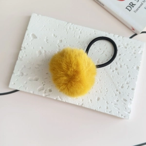 Close-up of yellow plush pom pom hair tie with high elastic band on a marble stone