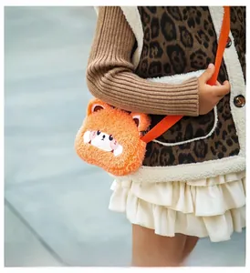 Detail of soft orange plush bear bag with embroidered face and crossbody woven strap