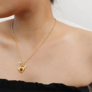 Detail of 18k gold heart necklace with red onyx and pearl on a model neck
