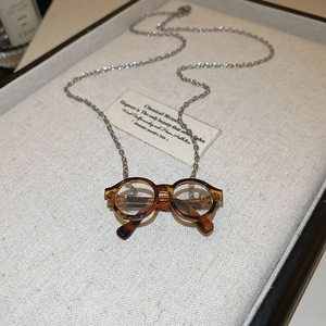 Close-up of a tortoiseshell sunglasses pendant on a silver chain over beige linen tray