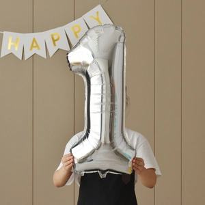 Silver number 1 foil balloon held for birthday party decoration against a grid wall