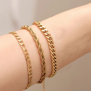 Gros plan de trois bracelets superposés en or : mailles Figaro, torsadée et gourmette