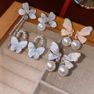 Asymmetric butterfly and pearl tassel earrings with diamonds on a velvet display tray