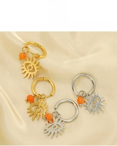 Detailed view of 18K gold and silver evil eye hoop earrings on beige satin background