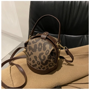 Detail of leopard print fabric and dark brown leather on a cylindrical bucket handbag