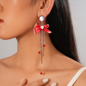 Close-up of red ribbon bow tassel earrings with heart-shaped gemstone and long crystal fringe