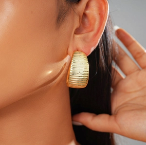 Detail of a woman wearing gold-toned C-shaped ribbed metal earrings with a polished finish