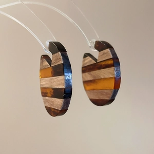 Macro view of C-shaped earrings with alternating dark wood grain and amber resin stripes