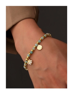 Detail of beaded shell bracelet featuring light green stones and gold-plated pendants