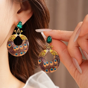 Detailed view of peacock earrings with green gemstones and colorful enamel feathers