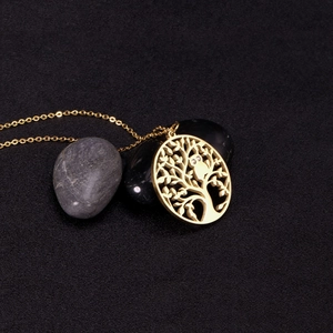 Detailed close-up of golden Tree of Life necklace with small owl pendant on dark stones