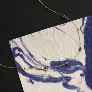 Dettaglio di perline dorate e perline blu scuro su una collana in acciaio inossidabile