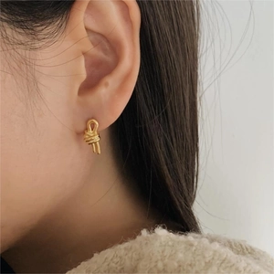 Close-up of elegant gold knot stud earrings worn by a model in a natural setting