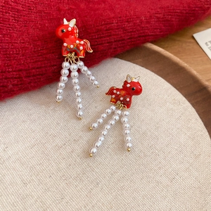 Macro shot of red enamel horse earrings with elegant white pearl tassel drops