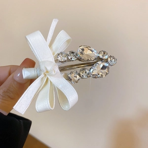 Détail d'une pince à cheveux en satin blanc avec cristaux brillants tenue à la main