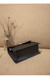 Detailed view of black leather bag base and golden chain strap on a soft fabric backdrop