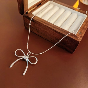 Silver bow pendant necklace resting on a vintage wooden jewelry box detail view