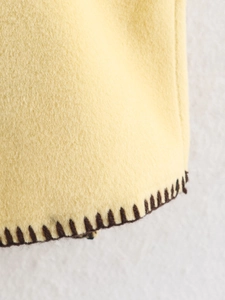 Close-up of yellow wool cloak fabric with brown contrast stitched edge detailing