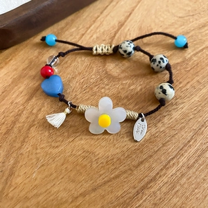 Détail d'un bracelet tissé à la main avec fleur en résine blanche et perles en pierre