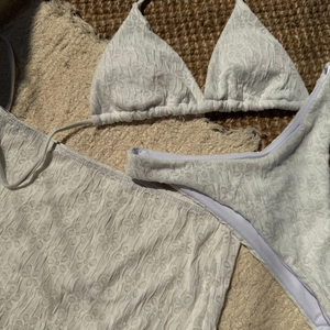 Detailed view of white three-piece bikini set featuring floral textured fabric and a sarong