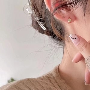 Close-up of small golden heart stud earrings worn by a model in soft lighting