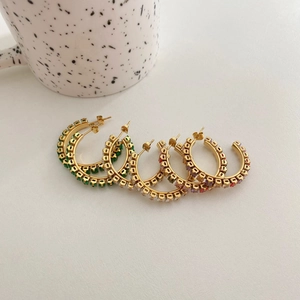 Detailed macro of gold hoop earrings with multi-color zircon stones on white surface