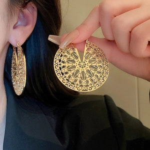 Detailed close-up of gold hollow-out disc earrings featuring intricate vintage patterns