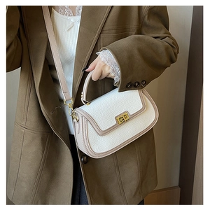 Détail d'un sac à main en cuir grainé blanc avec fermoir doré et bordures marron contrastées