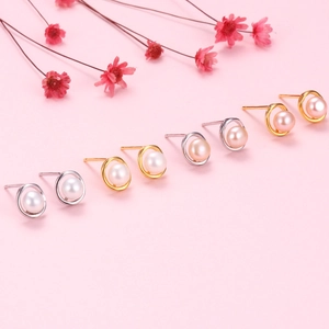 Close-up of pearl earrings in gold and silver circles over a soft pink floral background