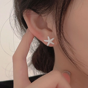 Detailed close-up of a silver starfish stud earring with textured surface on a model's ear